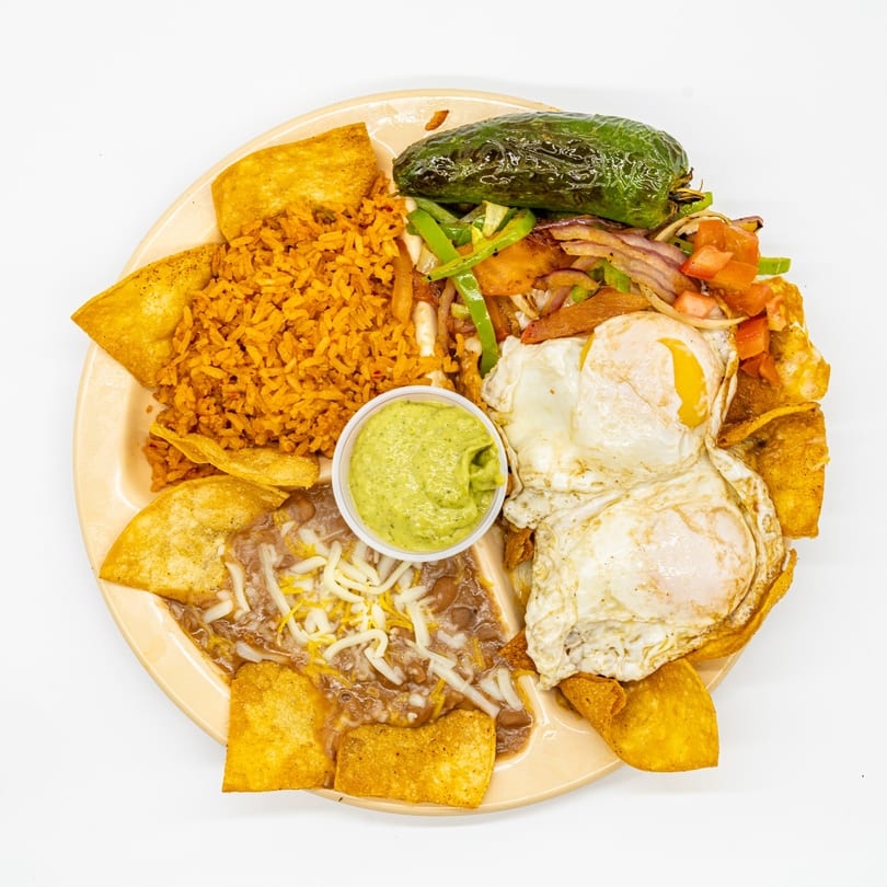 Mexican breakfast plate with fried eggs, rice, beans, tortilla chips, guacamole, and a grilled pepper.