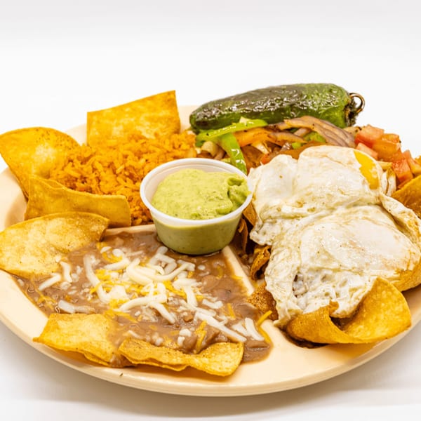 Mexican breakfast plate with fried eggs, refried beans, rice, tortilla chips, guacamole, and a grilled pepper.